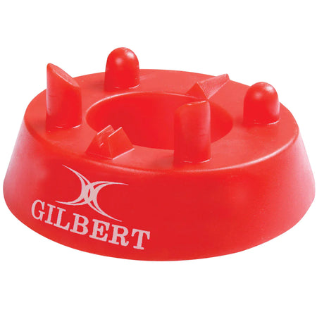 The Gilbert 320 Precision Kicking Tee is a red moulded rubber tee from Gilbert, featuring four raised prongs and a white Gilbert logo on the side, designed for accurate rugby kicking.