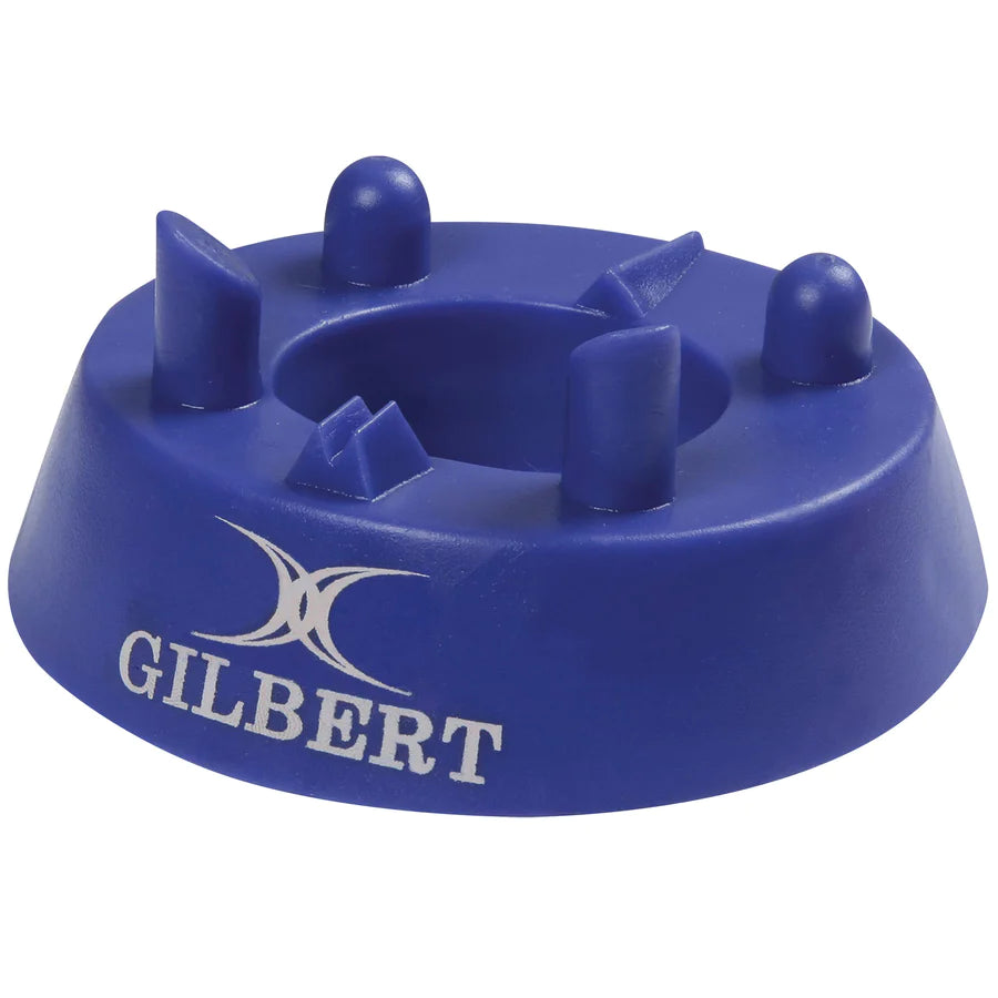 The Gilbert 320 Precision Kicking Tee is a blue moulded rubber tee with raised supports to hold a rugby ball upright. The white GILBERT logo and name are printed on the side.