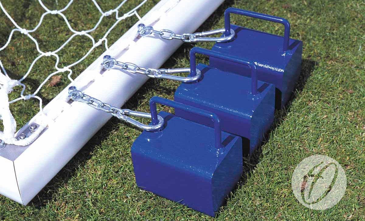 Three blue Harrod Sport Counterbalance Weight Anchors with handles are chained to the base of an aluminium goalpost on green grass, safely securing this freestanding sports equipment in place.