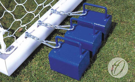 Three blue Harrod Sport Counterbalance Weight Anchors with handles are chained to the base of an aluminium goalpost on green grass, safely securing this freestanding sports equipment in place.
