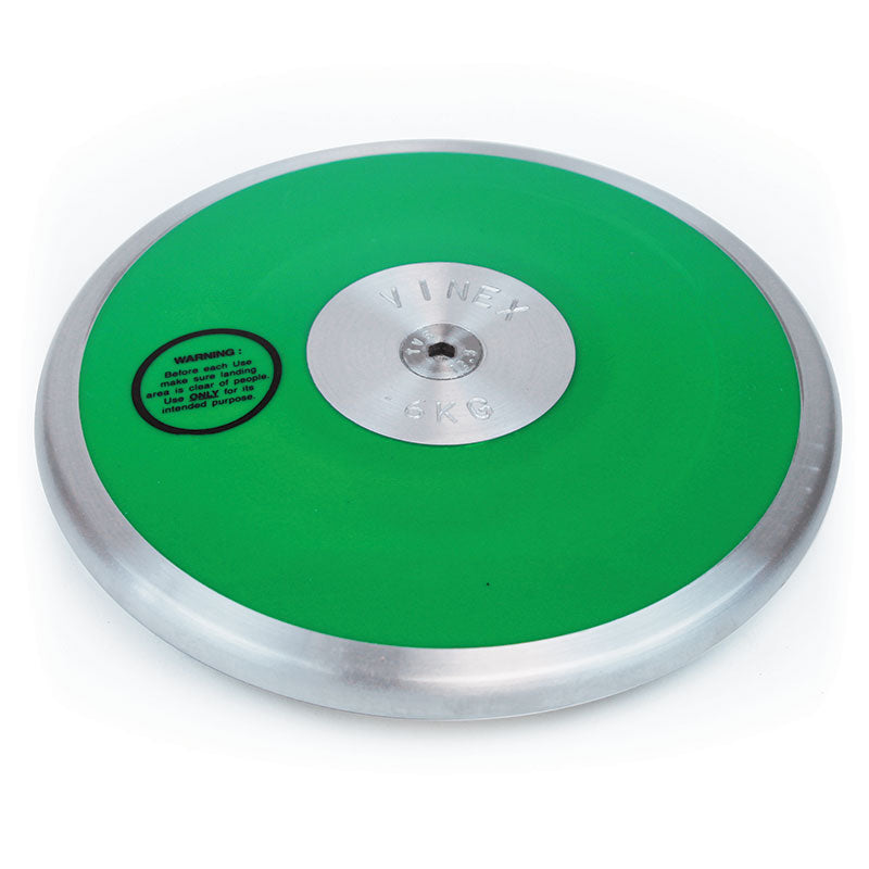 A green and silver steel rim Club Discus by Mastersport, featuring a metallic center and warning label on the left side. Weighs 5 KG, ideal for track and field events at schools or clubs.