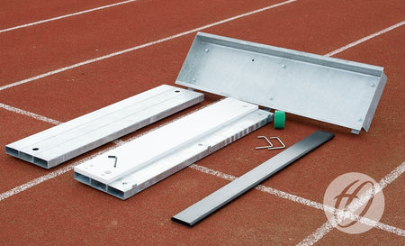 Harrod Sport Blanking Board and disassembled metal starting block parts are laid out on a red running track, with white lane lines visible in the background.