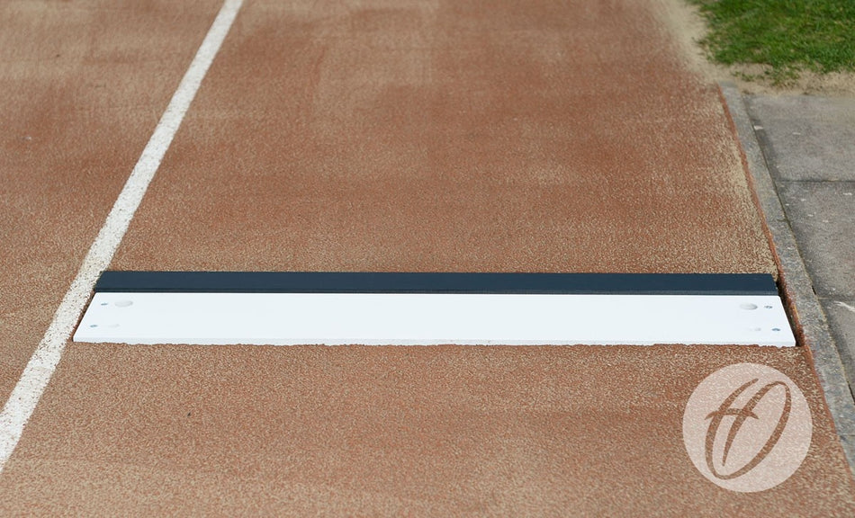 A close-up of the Harrod Sport Take Off Board, a heavy-duty galvanised steel long jump board, bordered by a white lane line on the track with green grass in the background.
