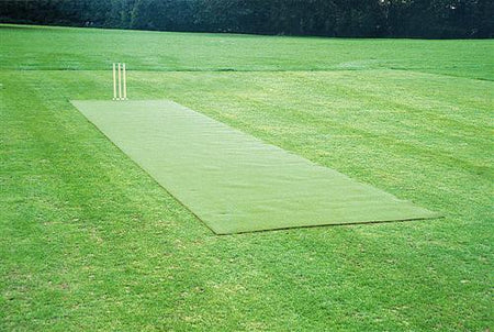 The Huck Nets Refurbishment of Artificial Wicket features a green mat cricket pitch with wooden stumps, set in a grassy field surrounded by trees—ideal for upgrading or maintaining artificial wickets.
