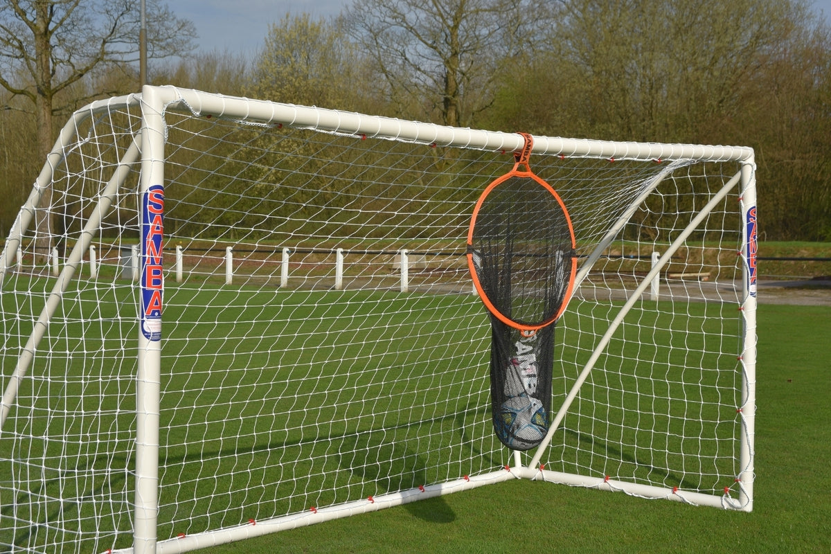 A Samba Sports Samba 2 in 1 Target Bag soccer goal stands on grass with a circular orange and black target net at its center. Trees and a fence in the background make it perfect for practicing your shooting skills.