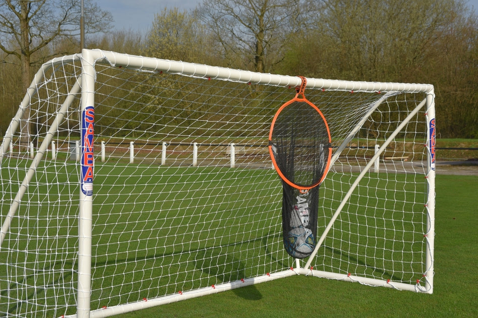 A Samba Sports Samba 2 in 1 Target Bag soccer goal stands on grass with a circular orange and black target net at its center. Trees and a fence in the background make it perfect for practicing your shooting skills.