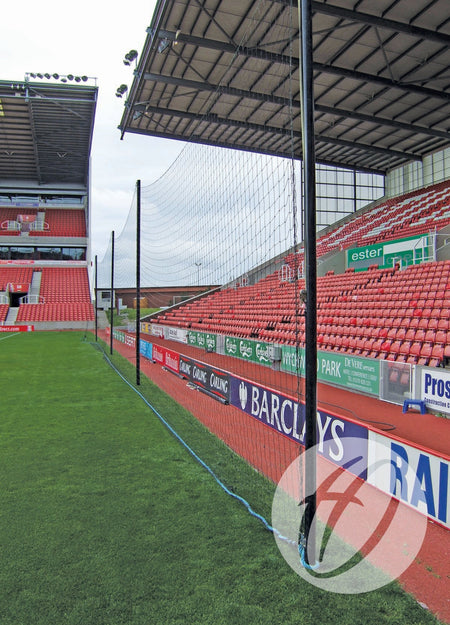 The Harrod Sport Crowd Protection Ball Stop System (50m x 5m) uses aluminium poles to support netting along the soccer field edge, separating the pitch from red-seated stands, with advertisement boards bordering grass and seating areas.