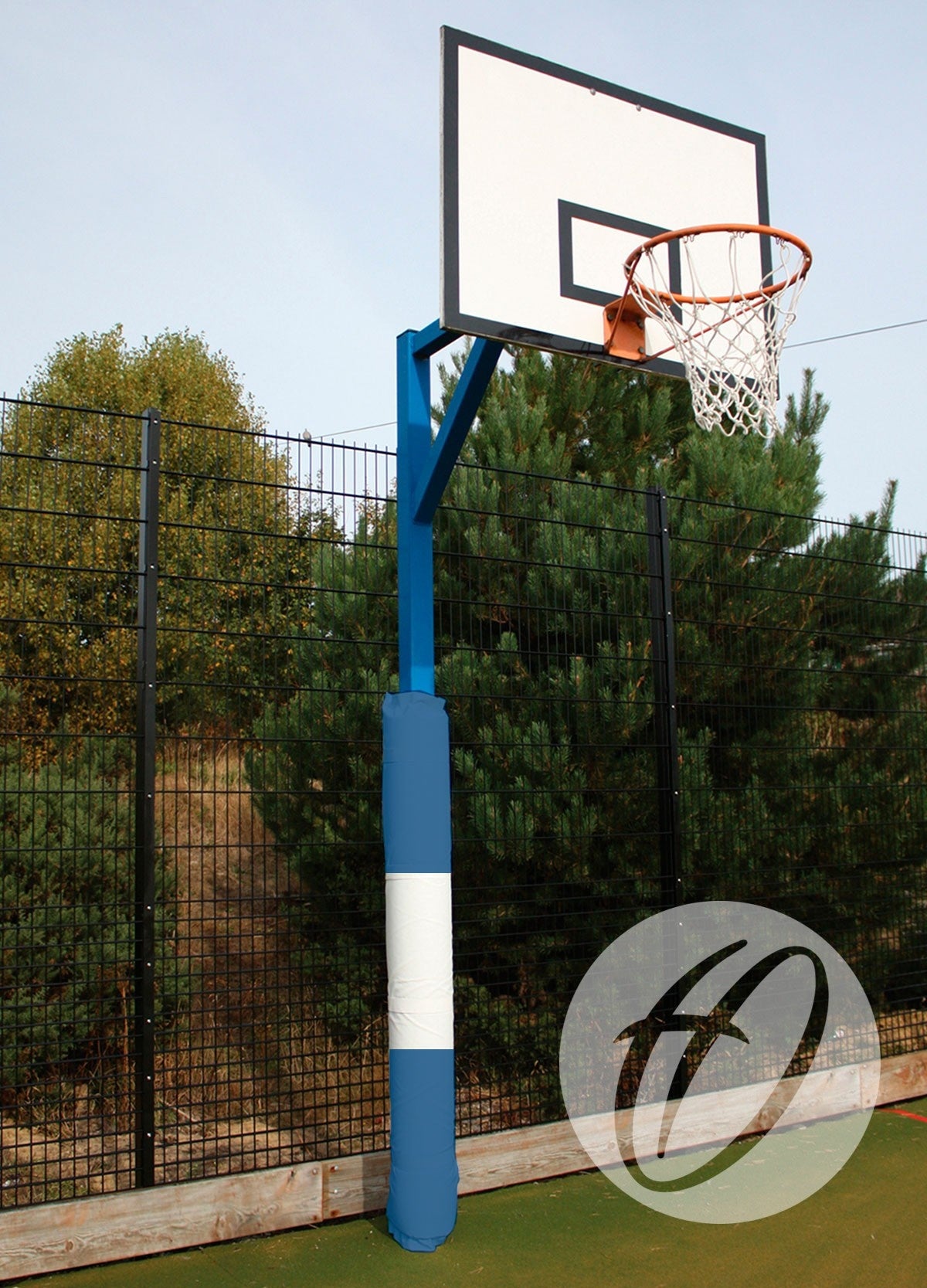 A basketball hoop with a white backboard and orange rim is mounted on a blue pole fitted with Harrod Sport Basketball Post Protectors – Multi Coloured. The outdoor court is near a fence and green trees.