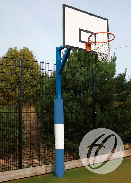 A basketball hoop with a white backboard and blue pole stands on an outdoor court near a fence and trees. The pole features Harrod Sport Basketball Post Protectors - Single Coloured, providing heavy-duty padding for added safety.