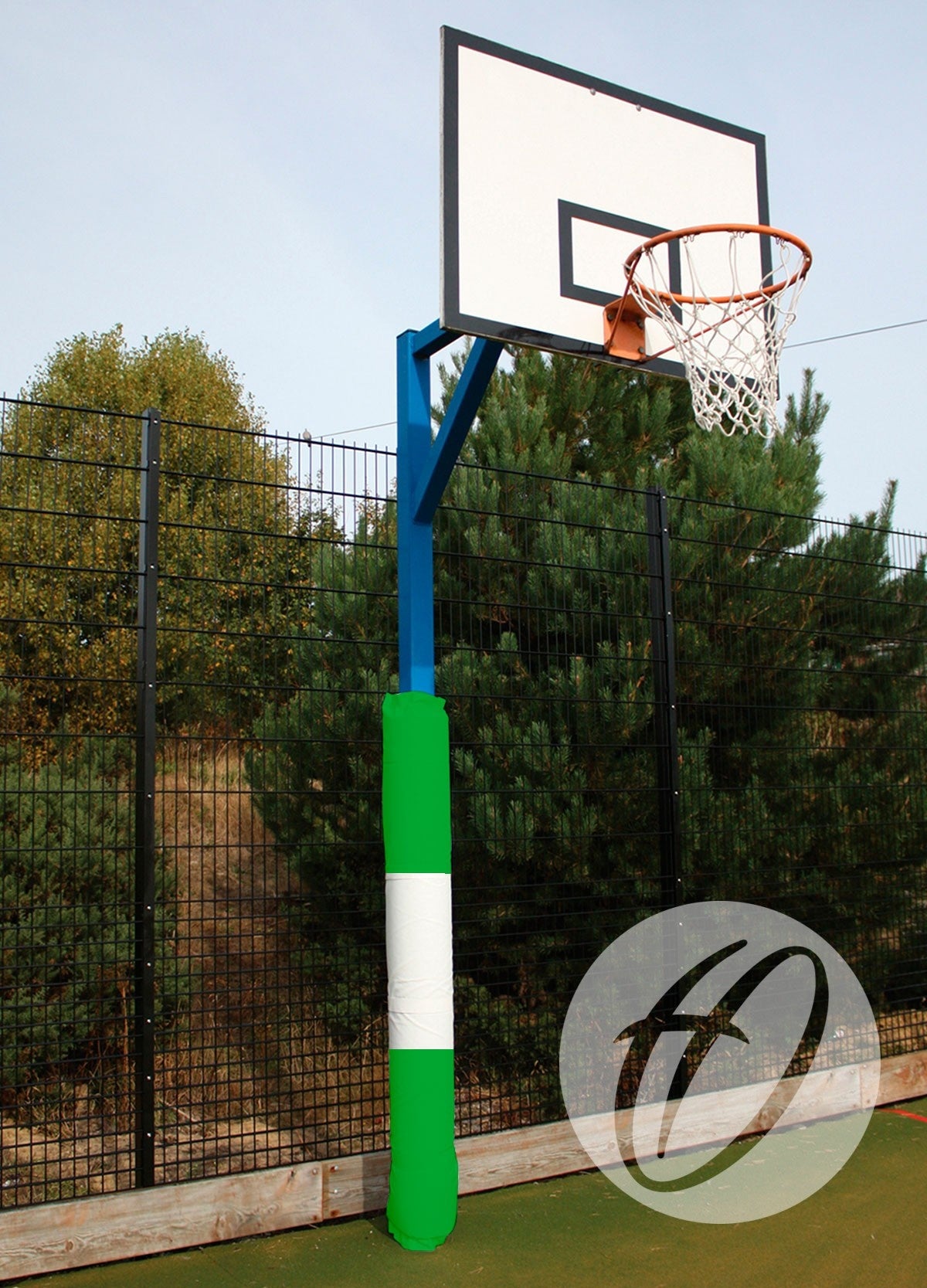 A basketball hoop with a white backboard and rusted rim stands outdoors by a tall black fence and trees. The pole is fitted with Harrod Sport Basketball Post Protectors - Single Coloured in green and white for enhanced safety.