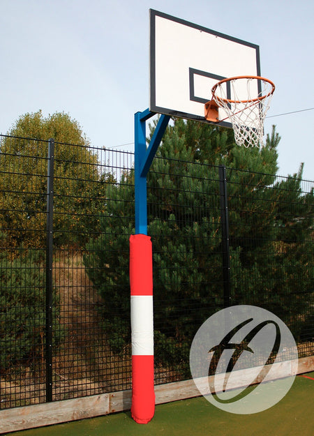 The Harrod Sport Basketball Post Protectors - Multi Coloured are wrapped around an outdoor hoop's pole, set on a court near a tall black fence and lush green trees.
