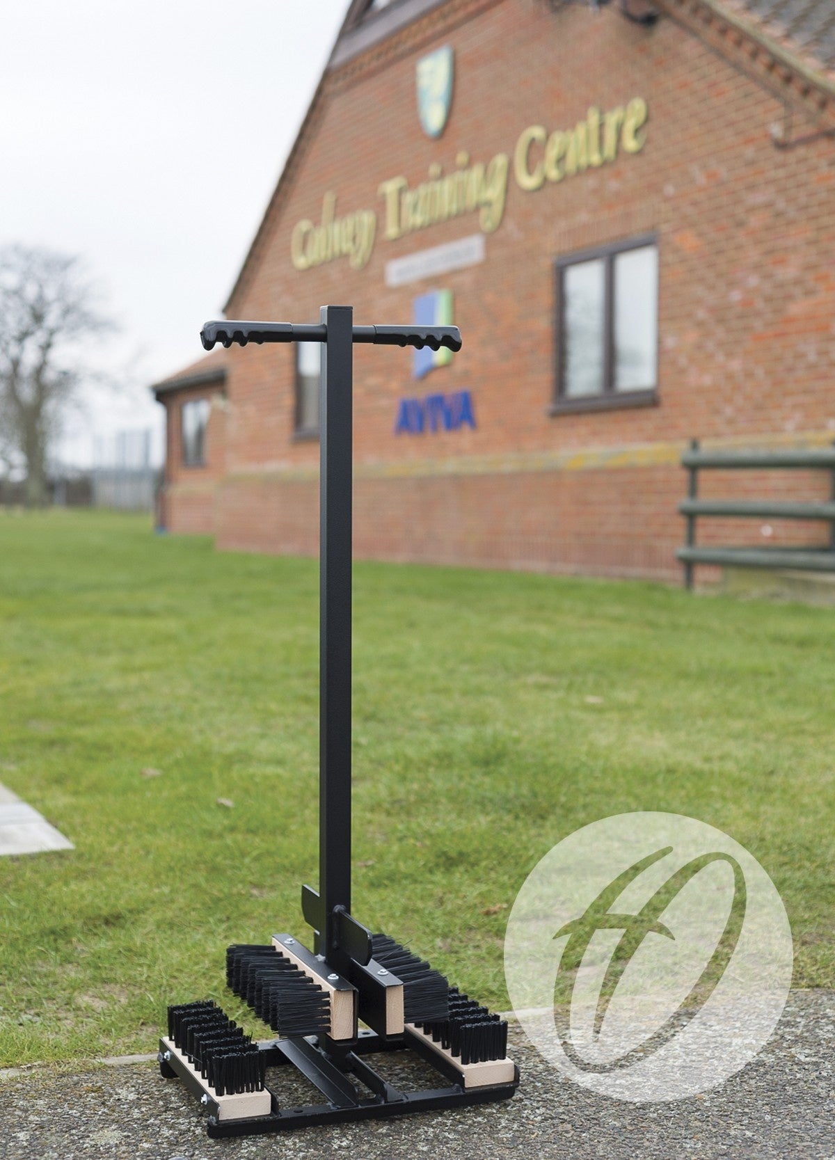 A Harrod Sport Standard Boot Wiper 1M with brushes and a handle stands on the grass outside a brick building marked Colney Training Centre, featuring the Aviva logo.
