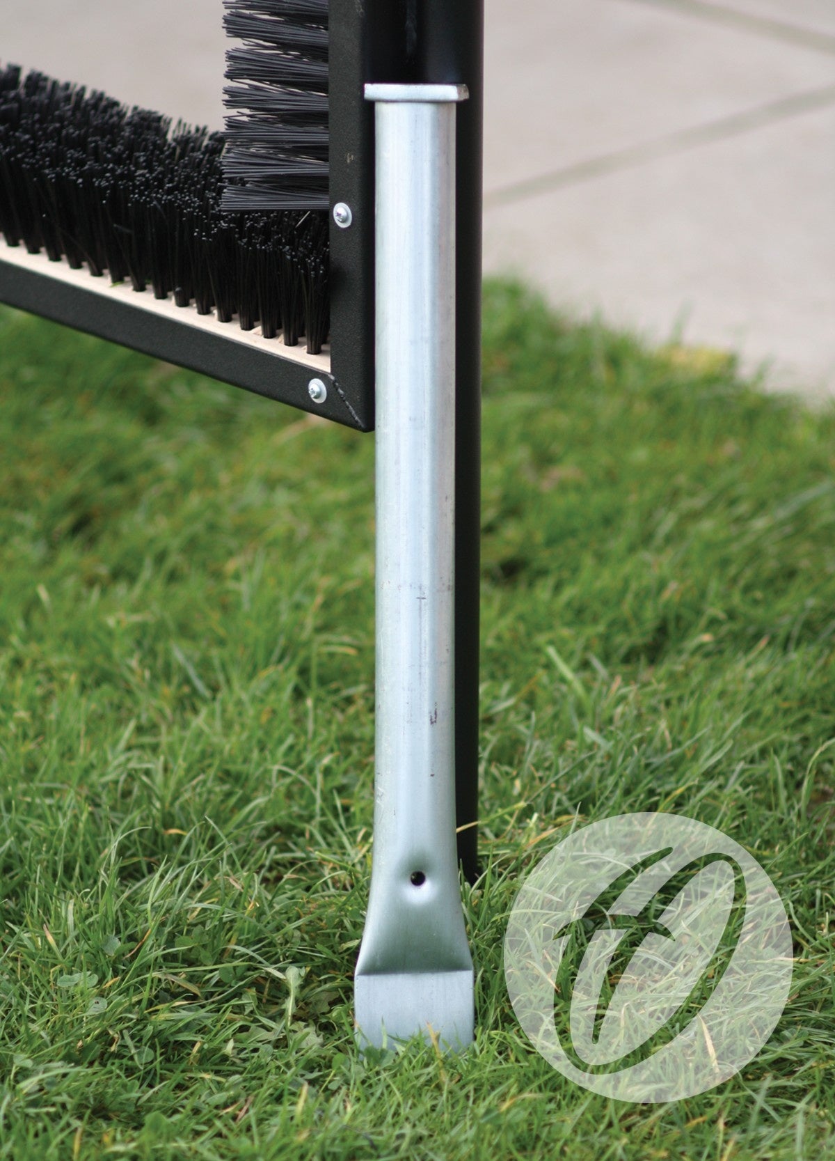 A close-up of a metal Socket For Multi Boot Wipers by Harrod Sport, supporting black-bristled units on green grass near pavement. A transparent circular logo appears in the lower right corner.