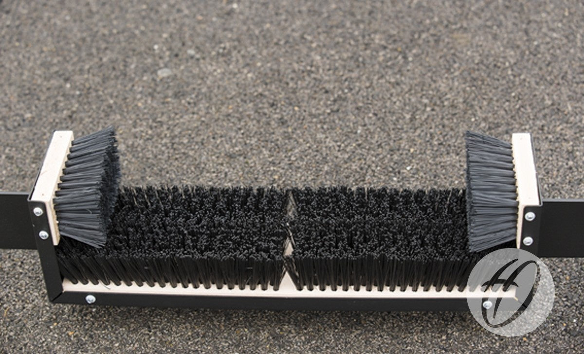 A close-up of the Harrod Sport Fixed Premier Boot Wiper 1.1m, featuring stiff black bristles mounted on a durable rectangular frame and positioned on a rough outdoor surface—perfect for placement near communal changing areas.