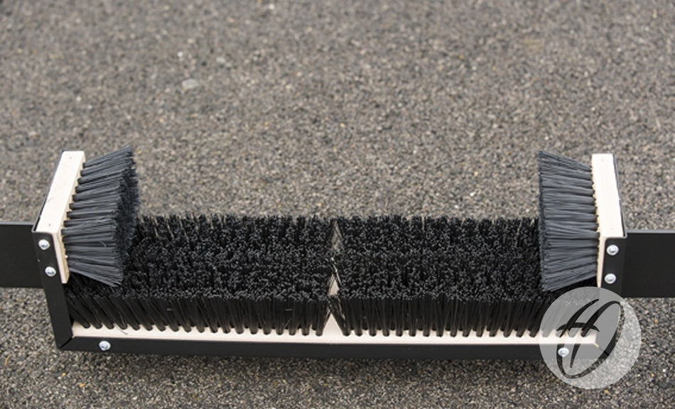 A close-up of the Harrod Sport Fixed Premier Boot Wiper 1.1m, featuring stiff black bristles mounted on a durable rectangular frame and positioned on a rough outdoor surface—perfect for placement near communal changing areas.