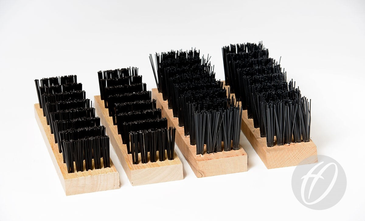 The Harrod Sport Spare Standard Brush Kit features three rectangular wooden blocks with rows of upright black polypropylene bristles, resembling oversized brushes. Displayed parallel on a white background, a circular logo with a stylized H appears bottom right.