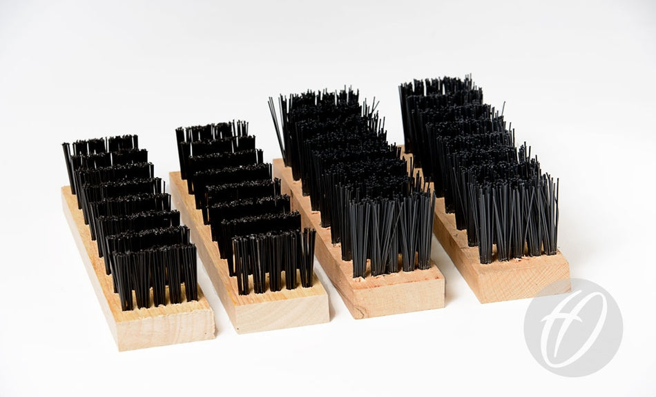 The Harrod Sport Spare Standard Brush Kit features three rectangular wooden blocks with rows of upright black polypropylene bristles, resembling oversized brushes. Displayed parallel on a white background, a circular logo with a stylized H appears bottom right.