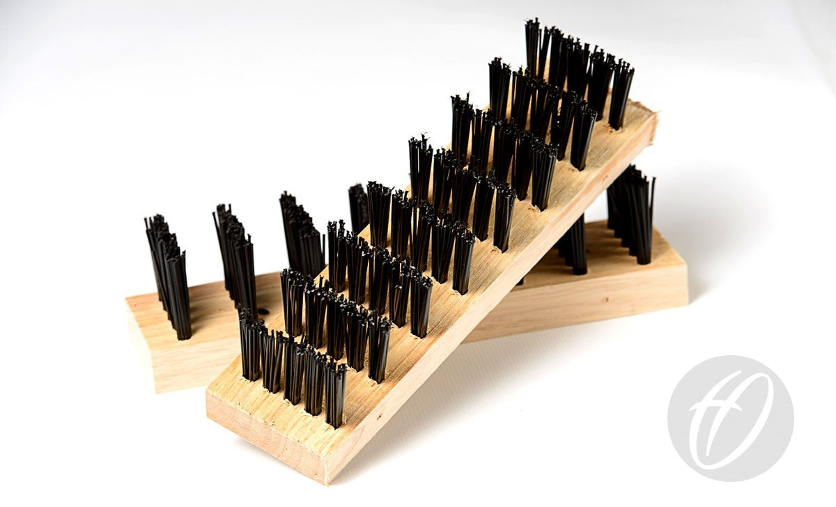 Two Harrod Sport Spare Standard brushes with black polypropylene bristles rest on a white surface, one diagonally atop the other. A gray circular Harrod Sport logo appears in the bottom right—ideal as a spare brush kit.
