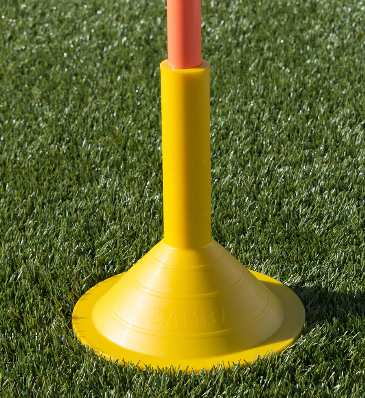 The Samba Sports Boundary Pole Base is a yellow plastic base (24cm diameter) that securely holds an orange pole upright on artificial green grass, ideal for sports training or marking.