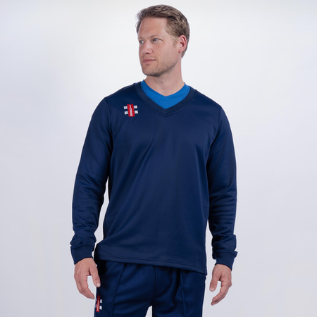 A man wearing a navy blue Gray Nicolls Monmouth CC Pro Performance Sweater and matching pants with small red and white logos stands against a plain light background, looking to his left with a neutral expression.