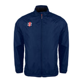 The Gray Nicolls Velocity Rain Jacket is a navy blue, water-repellent zip-up with a high collar, long sleeves, side pockets, and a small red and white chest logo. Its simple, sporty design is inspired by cricket.