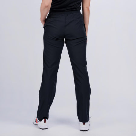 A person faces away from the camera, wearing Gray Nicolls Velocity Ladies Track Trousers by Gray Nicolls, a black top, and white athletic shoes against a plain light background.
