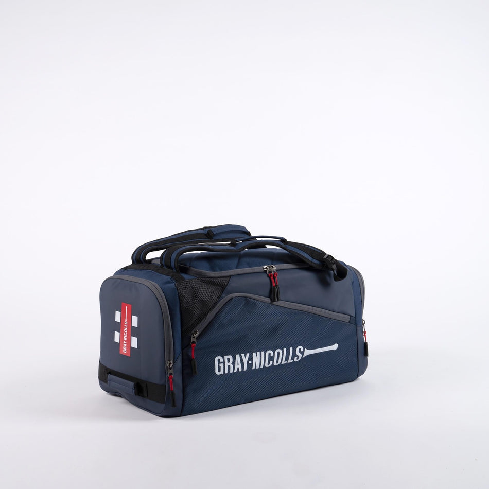 The Gray Nicolls Team Holdall 2026 is a navy sports duffle bag with black and red accents, branded with the Gray Nicolls logo. It features multiple zippered compartments, a shoe pocket, and padded handles for comfortable carrying.