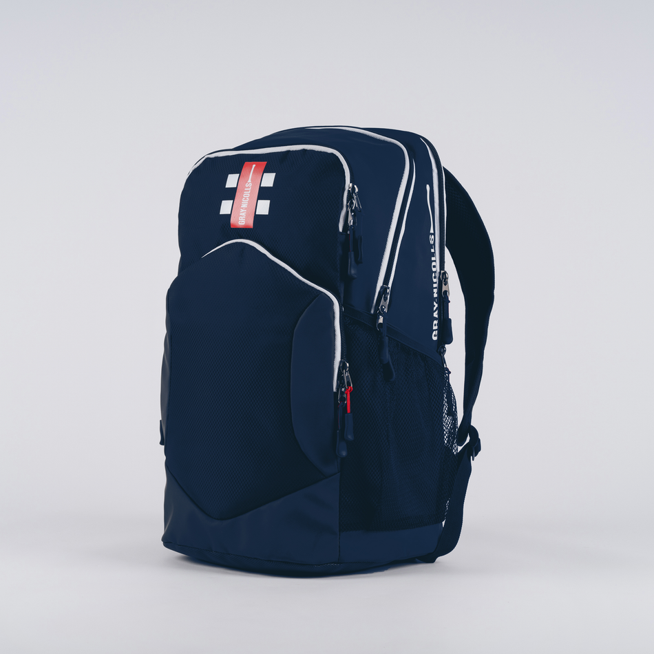 The Gray Nicolls Team Rucksack 2026 is a navy blue cricket bag with multiple zippered compartments, white accents, a mesh side pocket, and a red tag on top, standing upright against a plain white background.