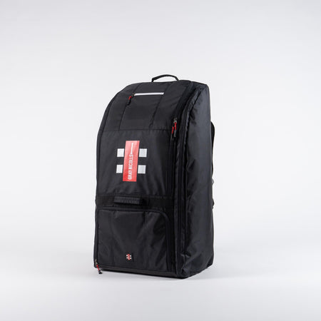 The Gray Nicolls Coach Bag 2026 is a large black bag with a top handle, red zippers, white rectangular accents, and a red GRAY-NICOLLS label on the front, shown upright against a plain white background.