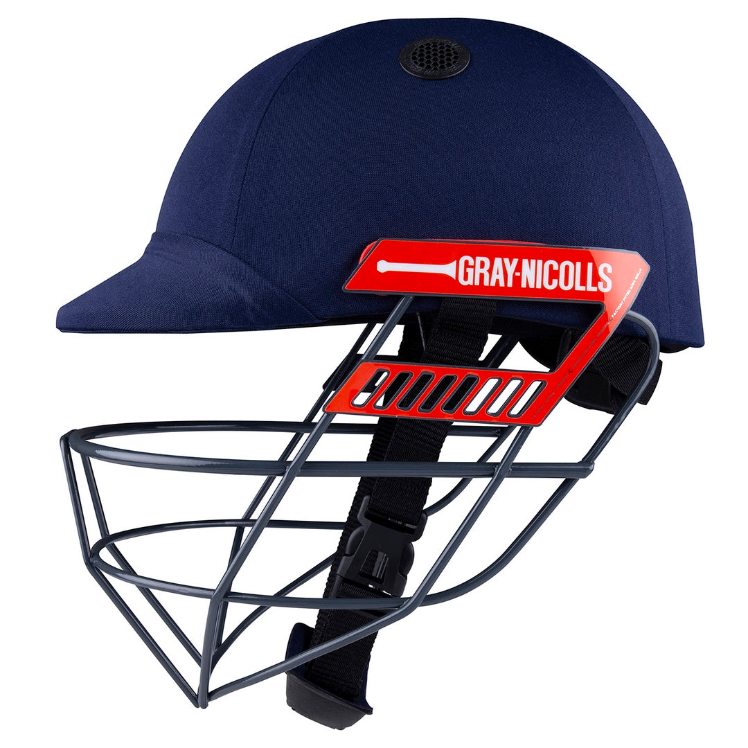 The Gray Nicolls Junior Ultimate Helmet in navy blue features a metal face guard, red side logo, and adjustable chin strap for a secure, comfortable fit.