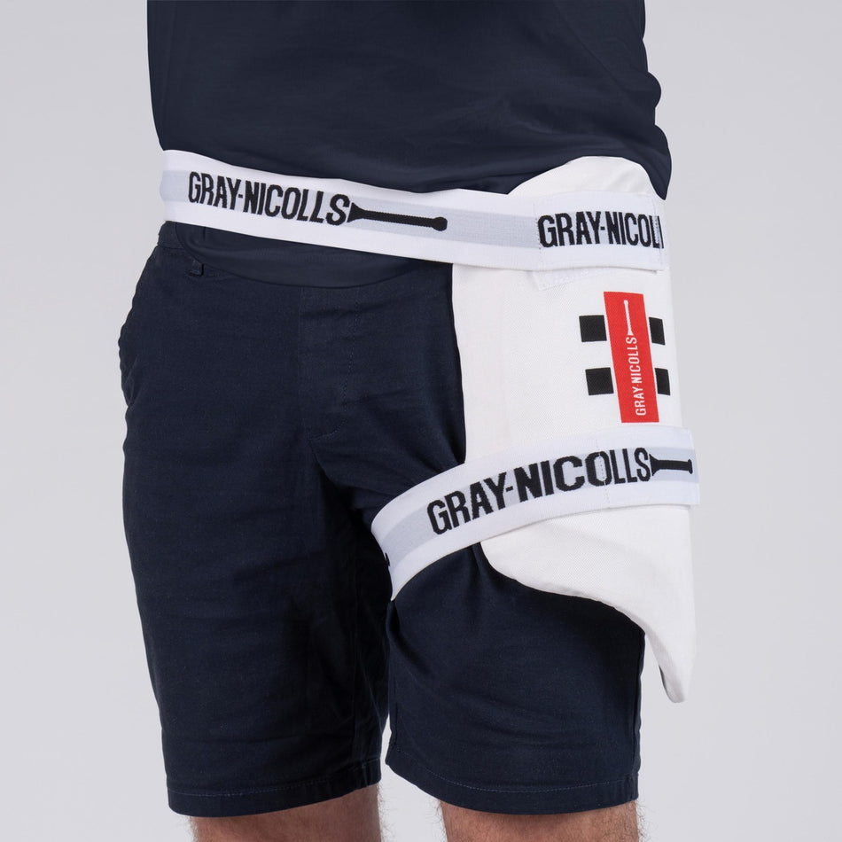A person wears the Gray Nicolls Club Collection Thigh Pad, featuring black straps, a red and black rectangular Gray Nicolls logo, and a breathable polyester cover for enhanced comfort.