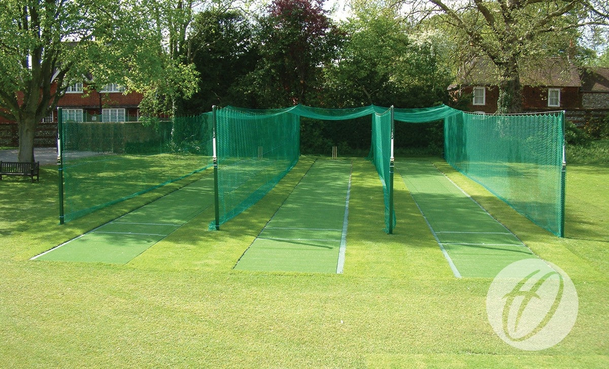 Four The Winch Cricket System - 3M Anchor Post nets by Harrod Sport with galvanised steel uprights and mesh enclosures stand on grass, bordered by trees and houses.