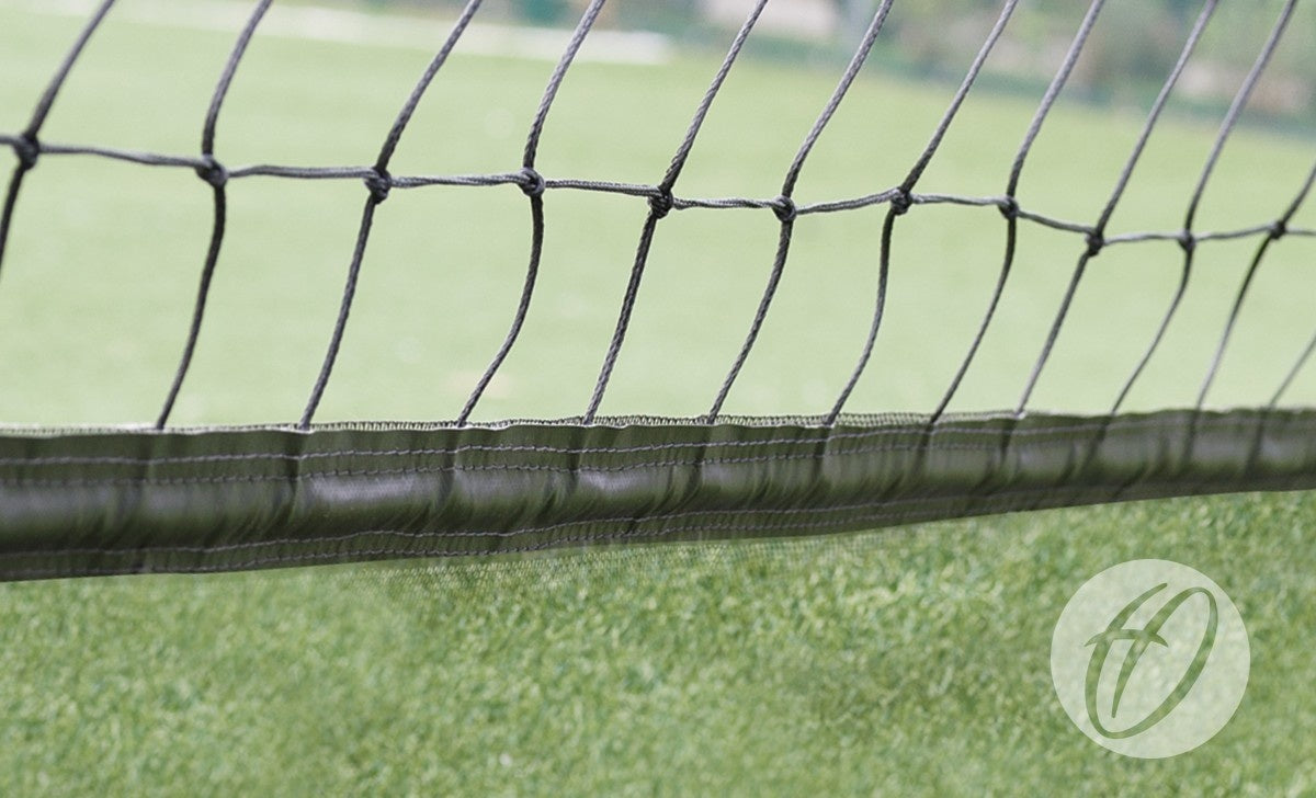 A close-up of Harrod Sport’s No16 Cricket Netting (2.7M high, 50MM band) shows the black UV-resistant polypropylene cords and stitched white top band, with green grass behind and a semi-transparent logo in the bottom right.