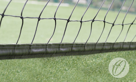 Close-up of Harrod Sport No.16 Cricket Netting - 3.6M High with 50MM band, made from UV-resistant black polypropylene, featuring a reinforced top edge and set against blurred artificial grass tennis court; circular logo bottom right.