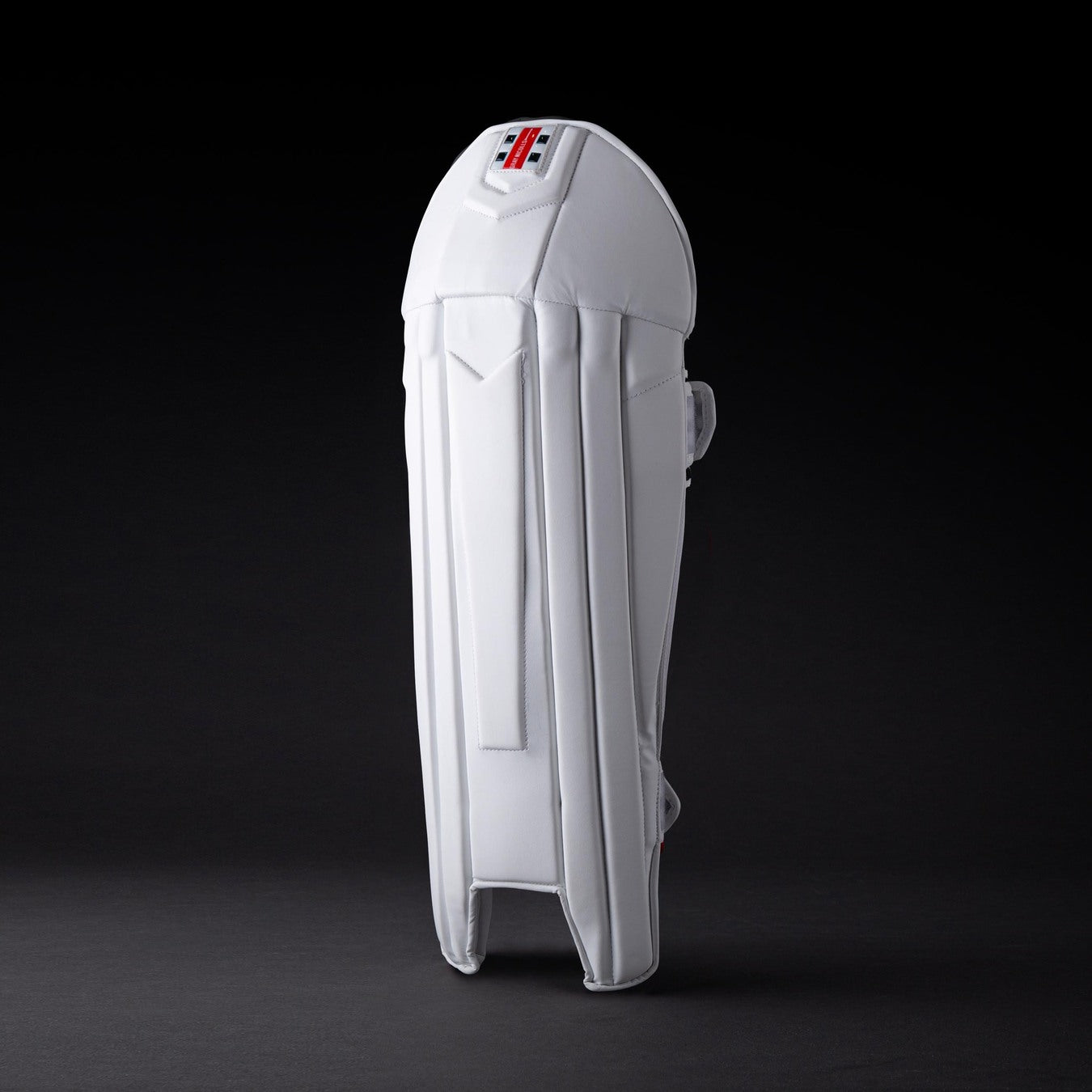 The Gray Nicolls Legend Wicket Keeping Pads 2026, featuring an ergonomic knee design and subtle logo near the top, stands upright on a dark background highlighting its white padding and secure straps.