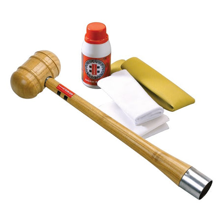 A Gray Nicolls Bat Conditioning Kit—including a wooden mallet, cleaning solution, white cloth, folded towel, and yellow textured cloth—lies on a white background: essentials for proper cricket bat maintenance.