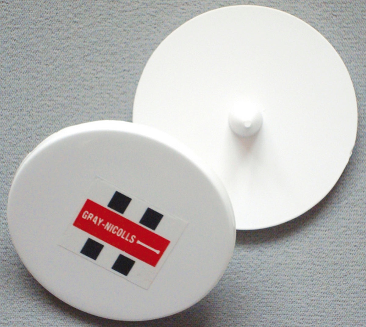 Two Gray Nicolls Bowlers Markers—one showing the red and black Gray Nicolls logo and the other revealing its central knob—rest on a gray surface, ideal for marking run-ups or use during training sessions.