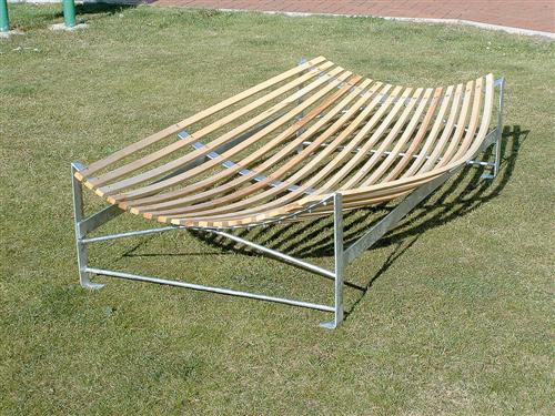 A set of Spare Laths for Catching Cradle by Martin Berrill Sports is shown on grass, evoking a modern bench with a curved, slatted wooden design and metal frame in a park-like setting.