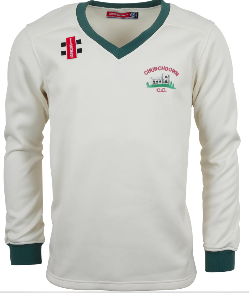 The Gray Nicolls Churchdown CC Pro Performance Sweater is a white long-sleeve cricket sweater with green cuffs and collar, a club logo and illustration on the left chest, and two black bars with a red rectangle on the right shoulder.