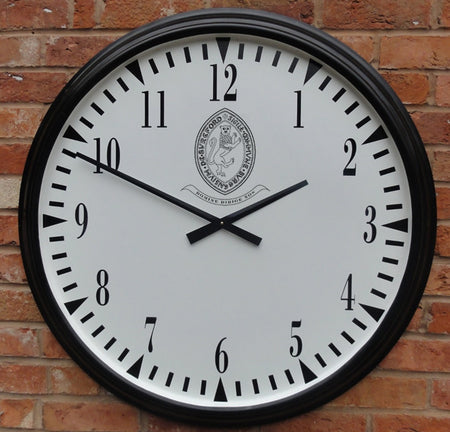 The Martin Berrill Sports Pavilion Sports Club House Clock features a large round white face with black numbers and hands set to 10:10, a crest with text at the top center, and is designed for external mounting on brick walls.