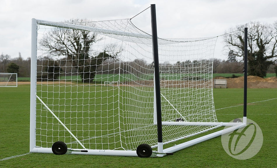 The Harrod Sport 4G Euro Portagoal - 7V7/5V5 is positioned on a grassy field. Its net is secured to a reinforced white aluminium frame, and two black support poles extend backward. Trees and cloudy skies form the background.