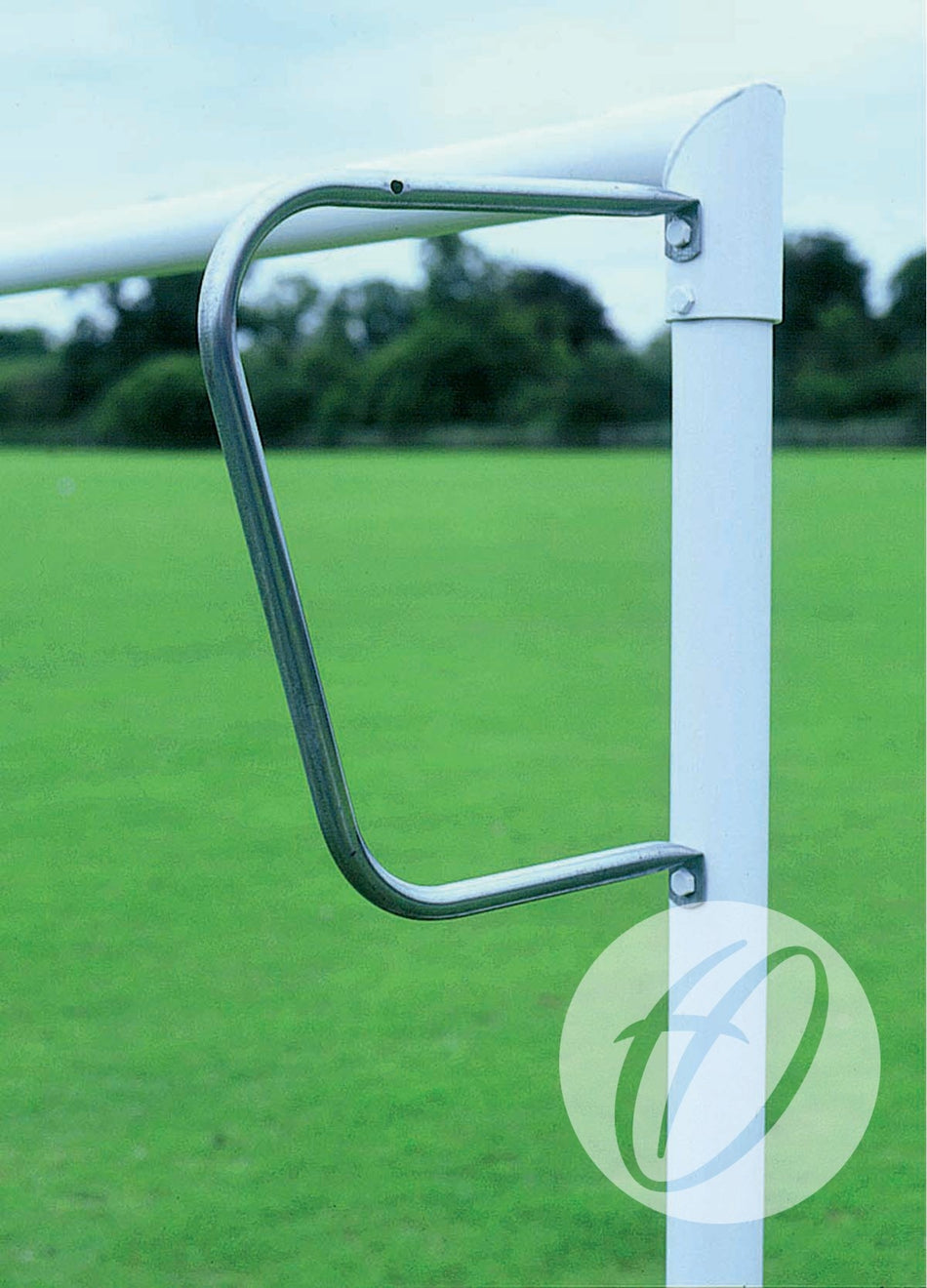 Close-up of a Harrod Sport Continental Tubular Steel Net Support for 9v9, 16x6, and 7v7 goals, attached to a white vertical pole on a green sports field, with trees and a cloudy sky in the background.