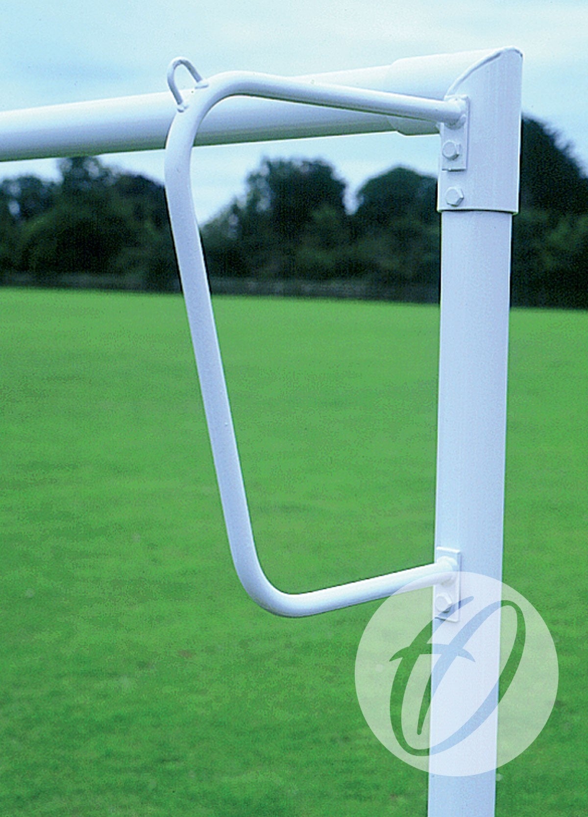 A close-up of a white Harrod Sport Continental Solid Steel Net Support attached to a goalpost on a grassy field, with trees and a cloudy sky in the background, highlights the robust steel construction and durability characteristic of net supports used for 9v9, 16x6, and 7v7 small sided goals.