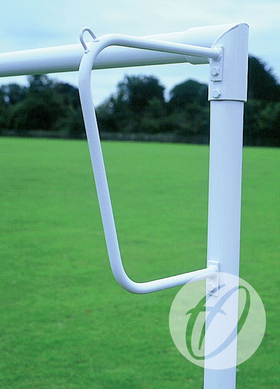 A close-up of a white Harrod Sport Continental Solid Steel Net Support attached to a goalpost on a grassy field, with trees and a cloudy sky in the background, highlights the robust steel construction and durability characteristic of net supports used for 9v9, 16x6, and 7v7 small sided goals.