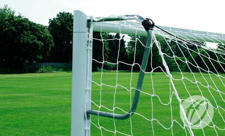 Close-up of a Harrod Sport 3G Mini Soccer Net Support - 9v8/16v6/7v7 on a well-maintained green field, with trees and a fence in the background under a clear sky.