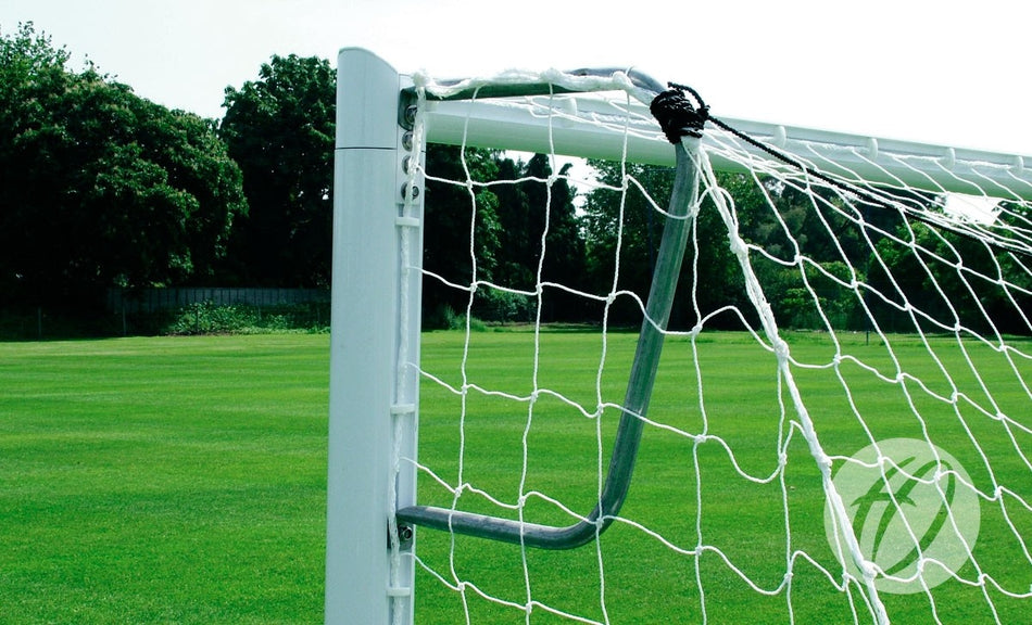 Close-up of a Harrod Sport 3G Mini Soccer Net Support - 9v8/16v6/7v7 on a well-maintained green field, with trees and a fence in the background under a clear sky.
