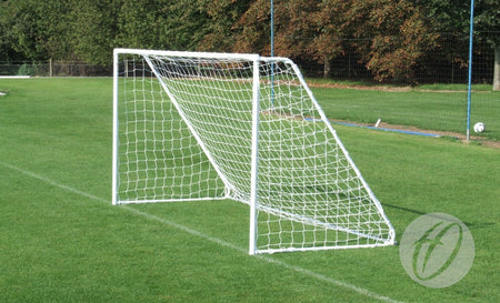 A Harrod Sport Freestanding Steel Football Goal (7v7/5v5) stands on a green grassy field, with trees and a fence in the background. The net is securely attached to the white, freestanding goalpost, and the field appears empty.