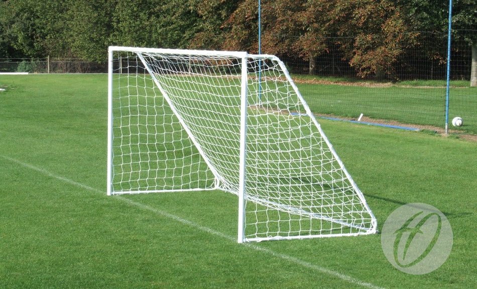 A Harrod Sport Freestanding Steel Football Goal (7v7/5v5) stands on a green grassy field, with trees and a fence in the background. The net is securely attached to the white, freestanding goalpost, and the field appears empty.
