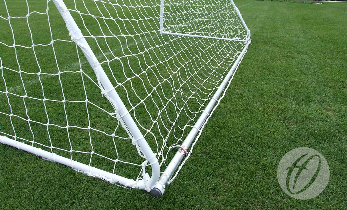 A close-up view of the Harrod Sport Freestanding Steel Football Goal - 7v7/5v5 and its net on a well-maintained grassy field, with a faint circular watermark in the bottom right corner.