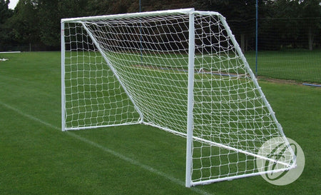 A Harrod Sport Freestanding Steel Football Goal, measuring 16′x6′, with galvanised steel back supports and a net is positioned on a green grass field. Trees and fencing can be seen in the background.